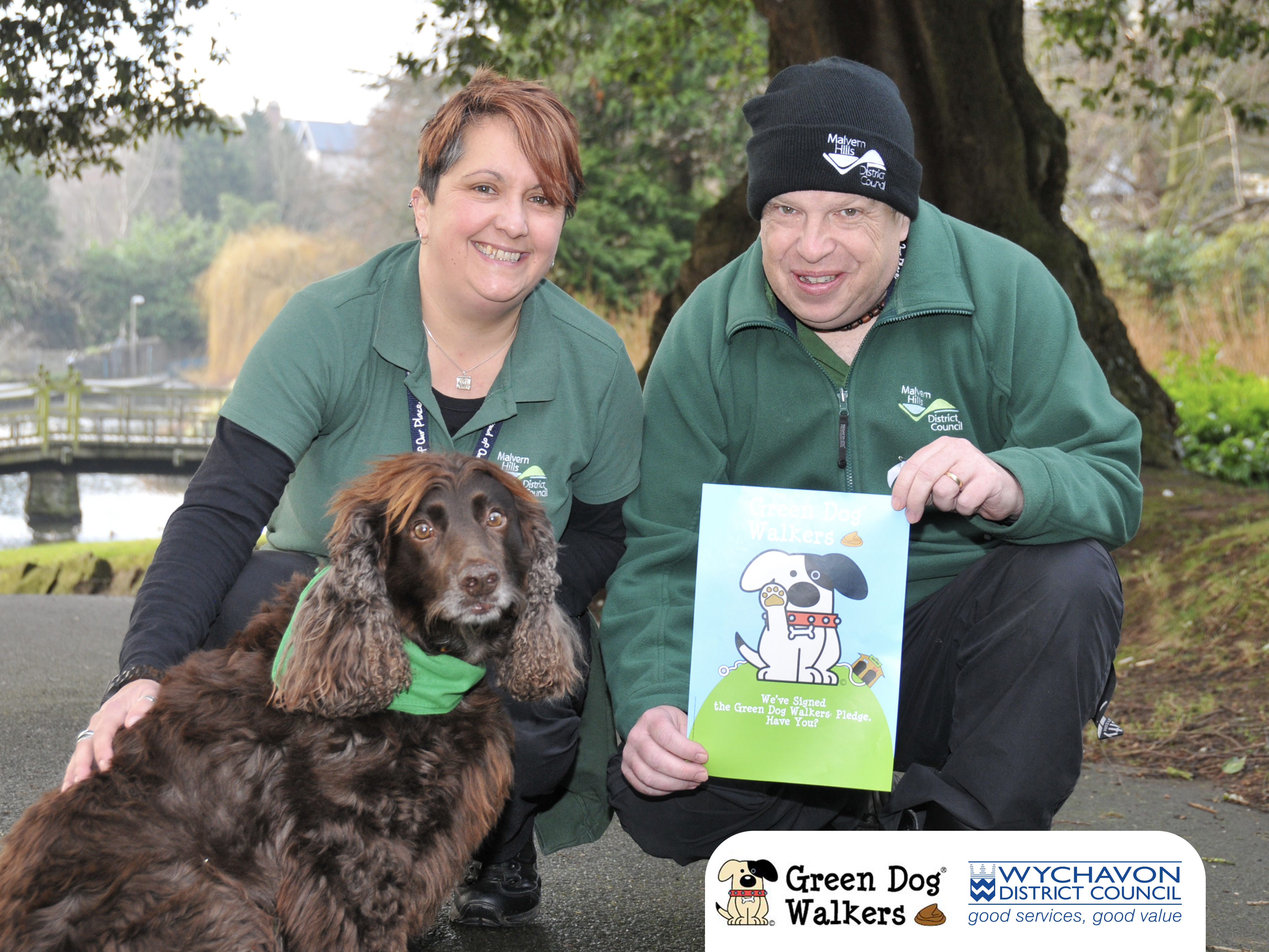 Man and woman posing with a dog and holding a poster