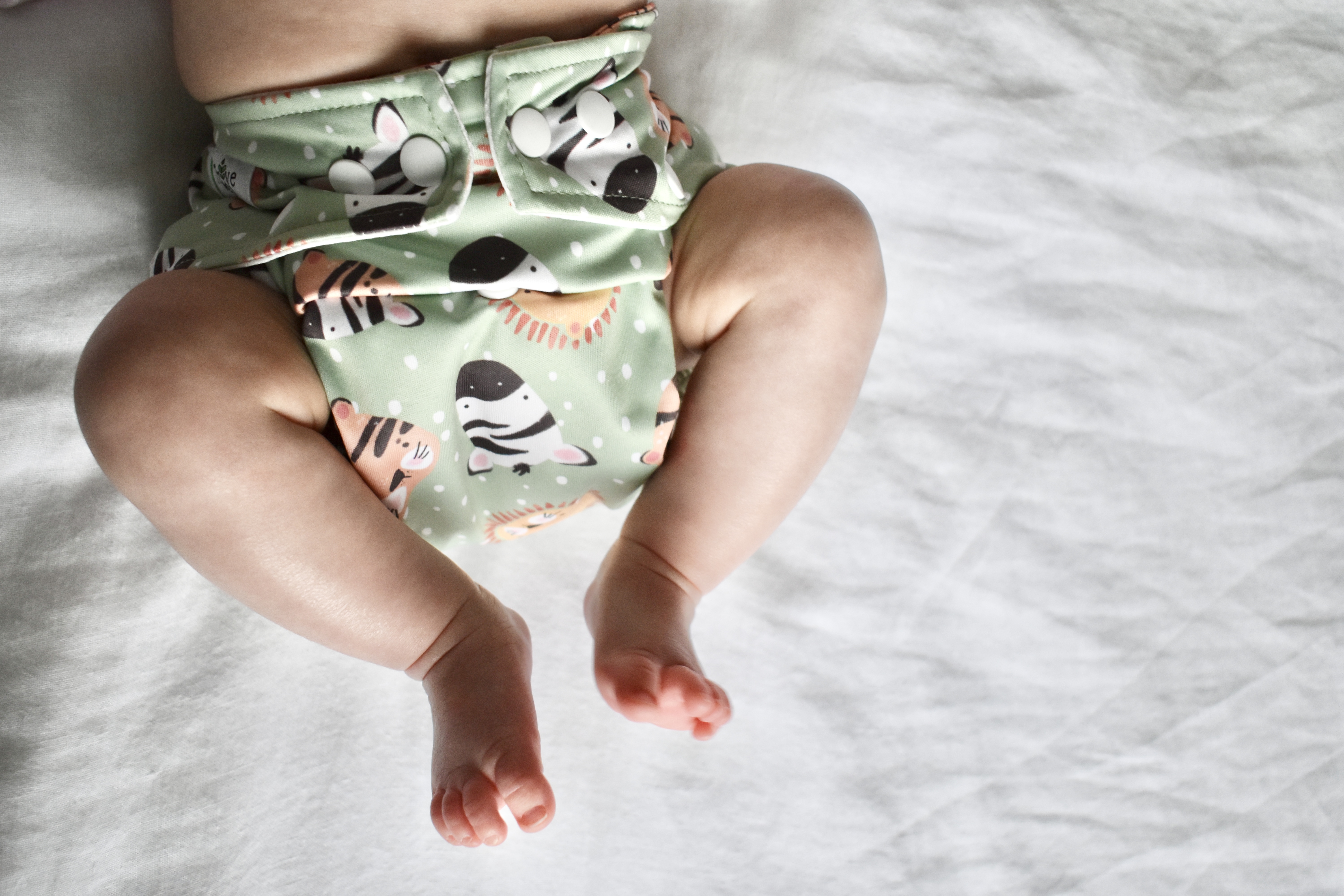 Image of the lower half of a baby, wearing a green animal print reusable nappy