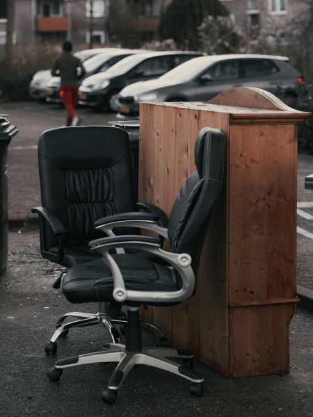 Two swivel office chairs and a wooden bookcase placed on a kerbside